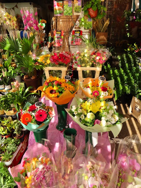A vibrant display of fresh flower bouquets arranged on green and white stems within a florist shop. The bouquets feature a variety of colorful flowers, including bright pink, yellow, orange, and white