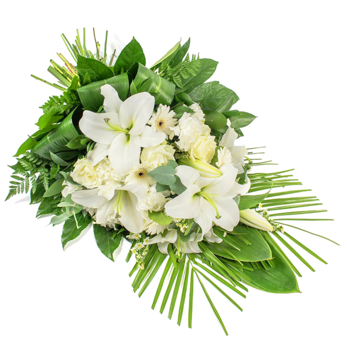 Set diagonally against a bright white background, this elegant funeral and memorial spray stretches in a fluid, teardrop-like line, composed almost entirely of white blooms and layered greenery that convey a deep sense of serenity. Large white lilies form the focal point, their trumpet-shaped petals open wide in some blooms, with gently rolled edges and soft shadows inside the flower throats, while others stand as elongated buds that hint at beauty yet to unfold. Around these lilies, clusters of white roses appear in various stages, from tight buds with smooth, ivory outer petals to semi-open flowers showing delicate, swirling centres. White gerbera-like daisies with pale yellow or cream centres add a simple, modern accent, their petals radiating evenly like small suns amid the composition. Ruffled white carnations and fine sprays of delicate filler blossoms fill the gaps, building a sense of volume and cohesion without ever feeling heavy. The entire spray is framed and shaped by a rich selection of foliage: broad, glossy dark green leaves are layered to form a firm base, feathery fern fronds soften the edges, and rounded eucalyptus leaves in subtle green-blue tones add an understated fragrance and visual calm. Some linear leaves are carefully folded and tucked to create refined structural lines. The most striking greenery is a sweep of long, slender palm fronds that fan out from the lower right, giving the spray its distinctive cascading outline. The overall mood is one of quiet respect and gentle remembrance, perfectly suited as a funeral tribute delivered to services and farewell gatherings throughout Gerrards Cross, from peaceful residential chapels to venues close to the leafy avenues near the station.
