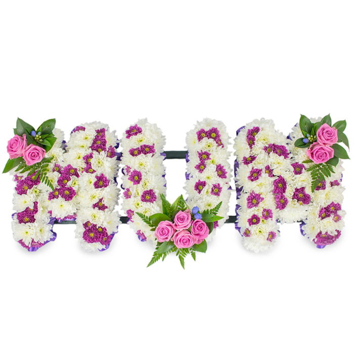 Set against a clean white backdrop, this bespoke sympathy arrangement spells out MUM in elegant, three-dimensional capital letters. The body of each letter is composed entirely of pristine white chrysanthemum blooms, packed tightly to form a luxurious, cloud-like surface whose small, layered petals invite a feeling of softness and solace. Interwoven among the white are tasteful patches of vivid magenta and purple spray chrysanthemums, which create subtle contrast and a gentle visual cadence across each letter. Three groups of vivid pink spray roses provide focal warmth: a small cluster crowns the upper left of the left-hand M, a more abundant bouquet nestles into the lower arc of the central U with several roses surrounded by fern and deep green foliage, and the right-hand M mirrors the left with a matching rose cluster at its top right. Delicate fern fronds and varied green leaves add texture and volume, while tiny blue accent flowers are used sparingly to lift the cool palette. The letters are connected by an unobtrusive dark horizontal support that maintains the arrangement's alignment and presence without drawing attention away from the flowers; a narrow purple ribbon traces each edge, giving the composition a refined finish. The overall effect is composed, respectful, and lovingly detailed-an intimate floral statement to honour a beloved mother at a funeral or wake, crafted with the considered touch of a local Gerrards Cross florist mindful of tradition, proportion, and the consoling power of flowers.