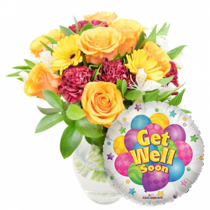 A cheerful and carefully balanced Get Well Soon arrangement, designed to convey optimism and gentle encouragement. The focal point is a lush cluster of roses in warm orange and deep yellow, their soft, velvety petals opening in layered spirals that feel reassuring to the touch even when only seen in a photograph. Bright yellow gerbera daisies scatter among the roses, their sunny discs and darker centres bringing immediate vitality, while rich burgundy and maroon carnations provide ruffled texture and a grounding contrast. Sprays of white alstroemeria punctuate the bouquet like tiny stars, their slender petals and delicate markings offering a refined highlight. Varied green foliage envelopes the flowers, glossy leaves and feathery stems giving the arrangement movement and a freshly gathered-from-the-garden impression; the clear glass vase displays the stems and water, a detail that speaks to freshness and professional preparation. To the lower right the bouquet is partially overlapped by a reflective round Mylar balloon; its silver surface showcases a playful cluster of illustrated balloons in purple, blue, pink, yellow and lime green, some decorated with polka dots or stripes. Bold yellow-and-blue lettering announces the message get well soon, framed by small colourful starbursts and a tiny KALEIDOSCOPE logo at the bottom edge. Made with bedside visits and doorstep deliveries in mind, this composition would be a thoughtful pick-up from a Gerrards Cross High Street florist or a comforting token for someone convalescing near The Green or in the surrounding Chalfonts.