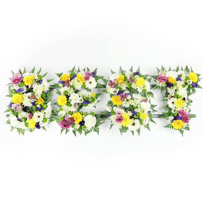 This carefully composed floral installation spells out the letters B, E, S, T in a bold, horizontal presentation against a stark white background, each letter densely trimmed with a mosaic of fresh, seasonal blooms and rich greenery. The dominant colour story is uplifting: golden-yellow roses and gerbera daisies provide radiant highlights, while generous white chrysanthemums and ivory gerberas lend soft, clouded texture. Scattered among these are clusters of pale mauve and deeper purple lisianthus or small chrysanthemums that introduce a contemplative, elegant tone, and pops of magenta-pink spray roses or carnations give subtle warmth and personal affection. Lush dark-green fern fronds edge the letters, their fine fronds softening the geometry and adding a natural frame; through a few tight spaces you can just make out the dark green structural bars that support the arrangement, especially across the E and along the lower part of the T. The photograph's frontal, even illumination reveals petal detail and the fresh sheen on leaves and blossoms, while the white backdrop heightens the colours' clarity. Designed as a sympathy or memorial tribute, the piece balances solemnity with celebration - a floral language that honours a life remembered as the best. As a Gerrards Cross florist I would suggest this for services near the station or for families gathering along Packhorse Road or in nearby Stoke Poges, and at Flower Delivery Gerrards Cross we often craft similar personalised letter tributes with the same attention to texture, scent, and proportion.