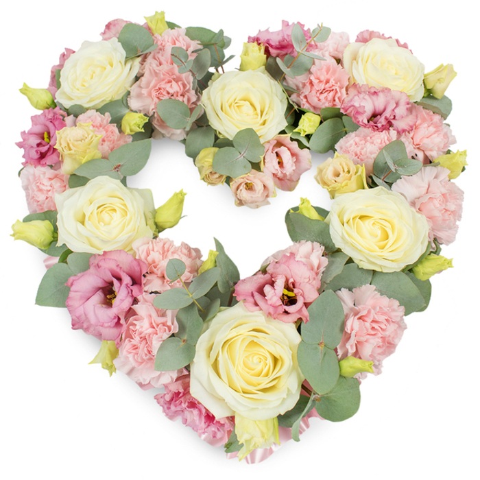 This image shows a meticulously crafted heart-shaped floral tribute, lying against an immaculate white backdrop so that every petal and leaf can be appreciated, much as it might look when delivered fresh to a service in Gerrards Cross. The heart is generous and full, the outline perfectly shaped and balanced, suggesting careful hands and years of floristry experience. Dominating the arrangement are large cream and pale yellow roses, their velvety petals tightly swirled at the centre and softening as they unfold, creating a sense of quiet elegance and enduring affection. Between these roses, clusters of light pink carnations add a gentle contrast, their famously frilled petals forming small, textured cushions that soften the overall look and evoke comfort. Deeper tones come from mauve-pink lisianthus blooms, some fully open and others still partially curled, with delicate, slightly rippled petals that introduce a graceful variation in shape. Small yellowish-green buds peek through the pastels, adding a hint of new life and subtle brightness. Threaded throughout are sprigs of silvery-green eucalyptus, their round to oval leaves adding depth and a cool-toned, calming base that frames the flowers and helps define the heart's curve. The composition feels both modern and timeless, an expressive piece that might be chosen as a central tribute at a funeral near West Common, or placed beside a framed photograph at a memorial gathering in a Gerrards Cross family home. It conveys love, sympathy, and remembrance in a way that feels gentle yet deeply sincere.