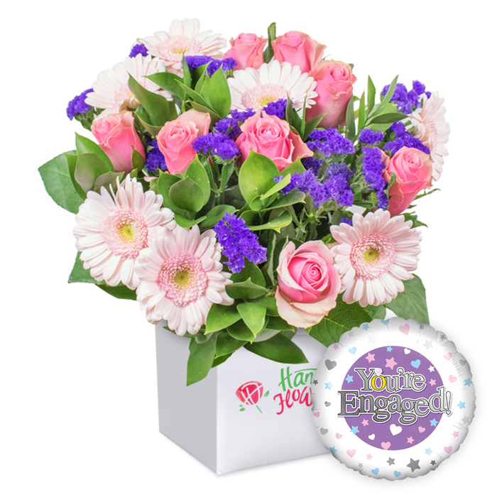 An artful, modern engagement bouquet sits in a pristine white square box, a vibrant testament to love assembled by a Gerrards Cross florist. The core is a cluster of full-bloom pink roses, their satin petals unfurling in soft spirals, paired with light pink gerberas whose edges glow with a gentle whiteness. Purple statice threads among the stems, providing jewel-like pops of color, while lush green leaves weave through to add depth and a garden-like mood. The box itself is minimal and bright, with a subtle emblem-a red rose graphic and green script-on its front, signaling quality from a local studio in Gerrards Cross. At the lower right corner, a round engagement-themed foil balloon floats, its lavender surface bearing a central purple circle with the message You're Engaged! rendered in shimmering silver, and a golden ring-shaped O catching the eye. The outer white rim is sprinkled with tiny hearts in pink, blue, and purple, punctuated by delicate silver stars, finishing the romantic celebration vibe. This arrangement makes a stylish gift to mark a proposal, a staple in wedding features, or to brighten a couple's home with freshness and hope. Delivered from our Gerrards Cross shop, it travels across the area for same-day arrival, a thoughtful gesture for celebrations near the village centre and beyond.
