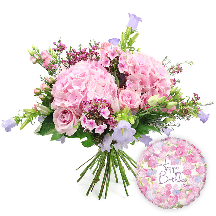 This image captures a joyful birthday gift set arranged against a clean, white background, showcasing the colours and textures of a hand-tied bouquet in soft pinks and purples, paired with a coordinating foil balloon. Dominating the centre of the frame, rounded clusters of pale blush pink hydrangea create a generous, cloud-like base, their countless tiny petals overlapping to form a plush, romantic mass that feels both modern and timeless. Among these sit graceful light pink roses, some fully open to reveal their classic swirling hearts, others still partially closed, suggesting unfolding moments of celebration in a home near Gerrards Cross Common or a quiet street off Packhorse Road. Scattered between the larger blossoms are delicate sprigs of deep pink or magenta waxflowers, or similar dainty filler, their tiny blooms and fine stems offering intricate texture and a subtle, sweet contrast to the softer tones. Rising slightly above the hydrangea dome, slender stems of campanula unfurl bell-shaped flowers in gentle lavender and periwinkle shades, adding a cool, airy lift and a hint of cottage garden charm. Surrounding the flowers, lush green foliage in varying shapes and sizes provides structure and a lively backdrop, emphasising the freshness one would expect from a bouquet prepared by skilled florists for same-day delivery across Gerrards Cross. The natural stems are gathered neatly at the bottom, clearly hand-tied and ready to be placed straight into a favourite vase. To the lower right of the flowers, a round, metallic Happy Birthday balloon catches the light with its subtle sheen. Its surface is adorned with an intricate floral pattern of small roses and buds in pink, cream, and lavender, echoing the bouquet's palette, while the central message Happy Birthday appears in elegant purple script. Together, the bouquet and balloon radiate warmth, joy, and thoughtful intention, ideal for celebrating a special birthday with beauty and grace.