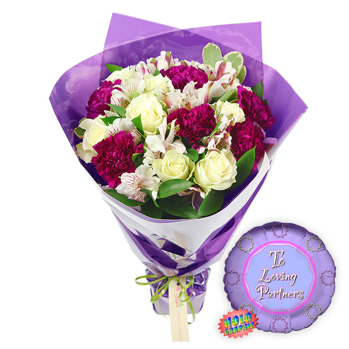 This image shows a lush and romantic bouquet paired with a coordinating balloon, styled against a pristine white background so every colour and texture stands out clearly. At the centre of the bouquet, several creamy white roses are arranged with care, their petals tightly layered into classic spirals that suggest both freshness and elegance. Surrounding and weaving between them are numerous deep magenta to burgundy carnations, their compact, frilled petals forming rounded, almost cloud-like shapes of intense colour that bring warmth and a sense of passion. Interspersed throughout are white alstroemeria, or Peruvian lilies, each bloom marked with fine reddish-brown lines and freckles on the inner petals, adding a delicate pattern that contrasts beautifully with the solid tones of the roses and carnations. The blooms are supported by a collar of vibrant foliage, including glossy green leaves and softly variegated greens edged in pale cream, lending depth and the feeling of a garden bouquet gathered from the quiet streets around West Common in Gerrards Cross. 

The florist has wrapped the stems in two distinctive layers. Closest to the flowers is a smooth, structured layer of crisp white paper that peeks out diagonally, giving the arrangement a clean, contemporary edge. Over this is a sheer, crinkled film of purple cellophane that rises gracefully around the blooms, creating soft reflections and a gentle, luminous sheen that echoes the bouquet's deeper purple tones. The stems are cinched at the base with a thin bright green satin ribbon, tied into a modest bow, from which hangs a small, rectangular light brown tag that appears ready for a personal dedication. Resting nearby on the white surface, to the right of the bouquet, is a round metallic purple foil balloon with a scalloped, rosette-like edge. In the centre, framed by a lighter lavender circle, the words To Loving Partners are written in elegant pink script, conveying affection and unity. A small rainbow holographic sticker clings to one side of the balloon, catching the light like a playful sparkle. The overall effect is of a carefully crafted romantic gift, ideal for anniversaries, Valentine's gestures, or simply saying I love you to a partner in Gerrards Cross and the surrounding Buckinghamshire villages.