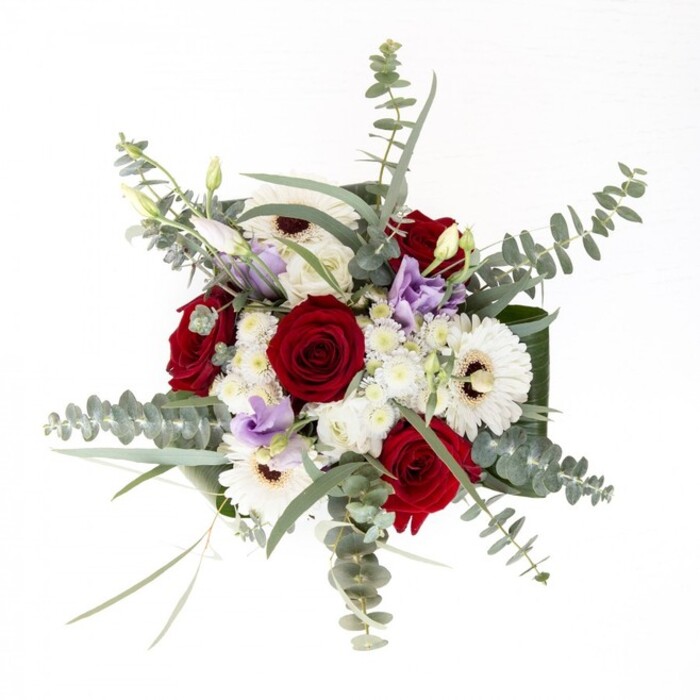This thoughtfully composed bouquet is a true showcase of floral artistry, capturing the sense of cultivated luxury unique to Gerrards Cross. Centered around several exquisite, velvety red roses-each rose a symbol of enduring affection-the arrangement is softened by the inviting expanse of white gerbera daisies. Their creamy petals, set around chocolate-hued centers, ground the bouquet with classic grace. Interspersed delicately are buds and blooms of soft lavender lisianthus, their presence gentle yet unmistakably contemporary. Eucalyptus, with its silvery-green, rounded leaves, lends both texture and a cool, faintly herbal aroma that whispers of the woodlands near Fulmer Road. Voluminous white filler flowers nestle lightly among the feature blooms, echoing the lightness of clouds drifting over Gerrards Cross Common. Framing it all, broad dark leaves sweep around the base, providing structure and focusing the eye upward. The water-filled glass vase allows the keen observer to appreciate the fresh, sturdy stems, an emblem of care and freshness. Designed for elegant home décor or heartfelt gifting on a local birthday or anniversary, this bouquet brings a refined sense of calm and beauty, as if drawn from the heart of a Gerrards Cross garden in full bloom.