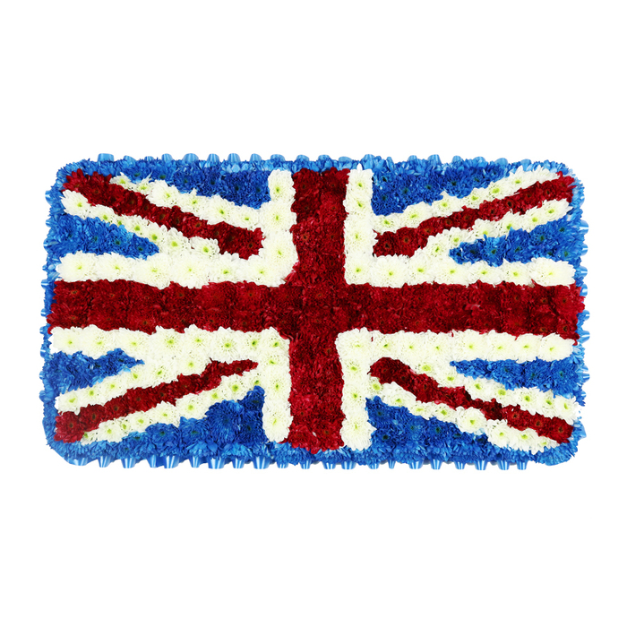 A detailed floral rendition of the United Kingdom's Union Jack flag is shown as a rectangular tribute, resting against a plain white backdrop that isolates its strong colours and careful structure. The entire piece is formed from numerous small, tightly clustered flowers, so close together that the surface appears almost velour-soft. Vivid red blooms, most likely short-stemmed chrysanthemums or similar pompom flowers, form the bold vertical and horizontal bands of St George's Cross at the very centre, their rounded shapes merging into a rich, uninterrupted stream of colour. Around these red lines, immaculate stripes of white flowers create the traditional fimbriation, their crisp petals defining the edges of every cross. Diagonal red pathways representing St Patrick's Cross intersect the central cross, framed on either side by generously wide diagonals of white to evoke St Andrew's Cross; the proportions are serenely balanced, giving the flag its instantly recognisable form. All remaining areas are filled with pools of deep blue blooms, possibly hydrangea heads or compact clusters of spray flowers, each one nestled tightly against the next so the background reads as a smooth, continuous field of blue. This deep colour frames the red and white beautifully, amplifying their brightness and echoing the tones of a clear evening sky above Gerrards Cross and the Chilterns. The meticulous craftsmanship gives the arrangement a slightly raised, three-dimensional quality, as if the floral flag might gently cushion the hand. Designed as a respectful funeral or remembrance tribute for services in Gerrards Cross churches, crematoria, or private memorials, it conveys solemn patriotism and heartfelt gratitude for the life being honoured.