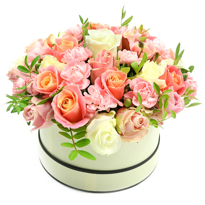 A sophisticated, lush bouquet presented in a round, cream-coloured hatbox that any Gerrards Cross customer would recognise as a thoughtful, premium gift. The hatbox has a smooth, matte surface and two subtle dark bands - one hugging the top rim and another low at the base - giving it a timeless, tailored look that lets the flowers remain the star. The arrangement rises in a full, domed shape of densely packed roses and carnations: the roses are a study in tonal transition, beginning with warm coral-peach and apricot at their hearts and fading to blush pink and creamy ivory at the petal edges, some opening wide and others kept as tender buds. Interspersed are delicate, ruffled baby-pink carnations that introduce soft, feathery texture and fill the spaces between larger blooms. Scattered sparingly among the flowers are slim sprigs of fresh green foliage with elongated leaves, providing subtle contrast and breathing room within the composition. Photographed against a stark white backdrop under even, natural light, each hue and petal texture is clear, emphasising the artisan skill of the arrangement. The overall impression is one of elegant abundance and heartfelt sentiment - a refined choice for birthdays, anniversaries, Valentine's Day or to mark special moments in homes around the Packhorse Centre, the High Street, or close to Gerrards Cross station. This particular presentation is arranged by Flower Delivery Gerrards Cross in our local studio, reflecting the town's preference for classic, well-crafted floral gifts.
