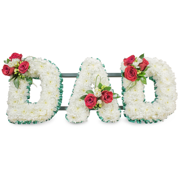 A carefully composed sympathy display spells DAD in three large capital letters, each letter densely covered with small, pristine white chrysanthemum blooms that give the surface a soft, full texture reminiscent of freshly fallen snow. The perimeter of every letter is trimmed with a deep emerald green pleated ribbon, the fine ridged detail of the ribbon providing a sculpted, formal edge that contrasts with the fluffy chrysanthemum heads. Placed with considered balance, rich red roses cluster on the upper curve of the left D accompanied by tiny white freesia buds and rich, dark foliage; the central A bears a matching arrangement positioned where the left diagonal meets the crossbar, with a graceful arc of bear grass reaching upward to introduce a contemporary line; the right D repeats the motif, mirroring the left for a cohesive triptych. A slim dark green or black metal support runs horizontally behind the letters, largely concealed by blooms but visible enough to hint at the piece's scale and structural care. The soft, even lighting and white background allow every petal, ribbon pleat and leaf to register clearly-textures, gloss and the slight velvety sheen of rose petals-while the fragrant interplay of roses and freesia brings a quiet sensorial comfort. Intended for memorial services, church displays or graveside placement in the Gerrards Cross area-near Burnham Beeches, Seer Green and the parish church-this tribute speaks of devoted love and profound respect, crafted with the precision of an experienced florist mindful of both aesthetic and ceremony.