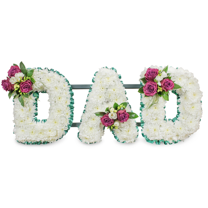 A striking, dignified funeral tribute spells out DAD in large, three-dimensional letters, each letter formed from a compact mass of pristine white chrysanthemum heads that together create a soft, voluminous texture resembling a blanket of pure petals. The letters are crisply framed with an emerald-green pleated ribbon that follows the outer and inner contours, the colour acting as a calm visual line that separates the white blooms from the surrounding space. A subtle dark green or slate-grey bar runs horizontally behind the letters, hinting at a sturdy easel-mounted display suitable for a church sanctuary or cemetery service. Carefully placed accent clusters add personal warmth: the first D is graced by a spray of deep magenta roses and small white freesia at its upper left; the A nestles its matching cluster low in the central V; and the final D mirrors this with a balanced grouping on the upper right curve. The roses range from tight buds to gently unfurling petals, their colour offering a rich, comforting counterpoint to the white chrysanthemums, while glossy foliage gives the arrangement weight and depth. In soft, neutral studio lighting the contrasts between texture and colour are clear; one can imagine the faint, clean scent of chrysanthemums layered with the sweet, honeyed notes of freesia and rose. This handcrafted lettering piece conveys solemn respect and tender remembrance - a classic and personalised choice for honoring a father at memorials in Gerrards Cross, Seer Green, and neighbouring villages.