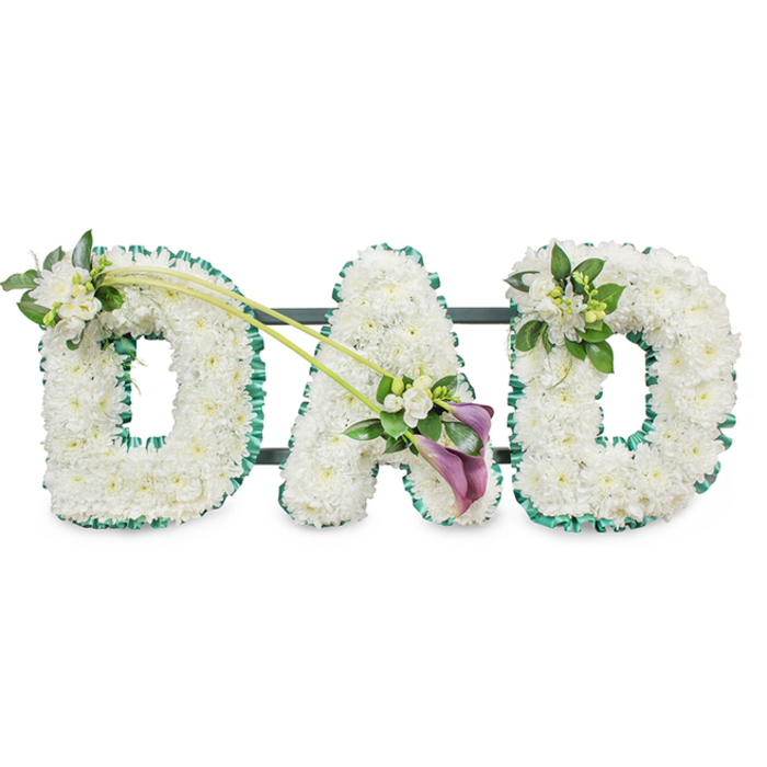 A striking funeral tribute in the shape of the word DAD stands out clearly against a bright white background, every detail reflecting the careful work of a professional florist serving the Gerrards Cross area. The three block letters are three-dimensional and robust, each one completely covered with a dense blanket of crisp white chrysanthemums or similar small button flowers. Their petals form a soft, cushion-like surface that looks almost cloud-light, creating a sense of purity and peace often chosen for final goodbyes at local churches and crematoria. Around the outer edges, a vivid emerald green ribbon has been meticulously pleated and attached, tracing every curve and corner of the letters and providing a strong, elegant contrast to the white blooms.   

The tribute is further enriched with artfully placed sprays of fresh flowers and foliage. On the upper left curve of the first D, a modest cluster of white freesia and glossy green leaves sits naturally on the chrysanthemum bed, bringing fragrance and gentle movement. From near the top of this D, two slender green stems sweep diagonally across towards the central A, almost like a bridge connecting the letters. At the point where they meet the A, an asymmetric focal arrangement draws attention: two deep purple calla lilies, their smooth, flared trumpets turned slightly outward, are nestled among more white freesia and lush green foliage. This rich, velvety purple accent introduces a note of solemn beauty and emotional depth, echoing the quiet dignity of farewells held near West Common or down the tree-lined roads of Gerrards Cross. The final D carries a smaller, complementary cluster of white freesia and greenery on its upper right edge, bringing the design into visual balance.   

Subtle dark support bars can be glimpsed behind the letters, indicating a sturdy frame designed for display beside the coffin, at the graveside, or on a stand during a memorial service. Overall, this DAD floral tribute conveys love, respect, and heartfelt remembrance, a deeply personal expression of loss for a cherished father.