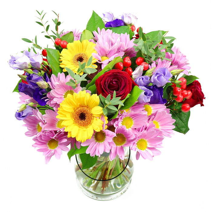 In a simple clear glass vase, a full and colourful bouquet rises like a small garden, photographed against a plain white background that sets off each bloom. At its centre, rich red roses unfurl in velvety spirals, creating a deep, romantic core that anchors the entire design, much like the historic charm at the heart of Gerrards Cross. Flanking these are two bright yellow gerbera daisies, each with a dark, earthy centre that glows warmly, suggesting optimism and happiness. Spilling outward from the middle, soft pink daisies or chrysanthemums form generous clusters, their many slender petals and tiny yellow centres building a feathery, cushion-like layer of pastel colour. Threaded gracefully among them are stems of purple and lilac lisianthus, their bell-shaped blooms and gently ruffled petals lending an air of refined elegance and cool sophistication, as if echoing the calm, tree-lined streets around West Common. Scattered throughout are bright red Hypericum berries, small and round with a glossy finish, bringing playful pops of texture that catch the eye and hint at changing seasons. The bouquet is wrapped in a variety of green foliage: some leaves are broad and dark, lending structure and depth, while others are slender, lighter, and more delicate, softening the edges and making the arrangement feel naturally abundant. Inside the transparent vase, neatly trimmed stems are visible, standing in clear water, showing the florist's attention to detail and careful conditioning of each flower. The overall impression is of a joyful, thoughtfully composed gift-perfect for birthdays, congratulations, or a warm thinking of you sent to a home or office anywhere across Gerrards Cross.