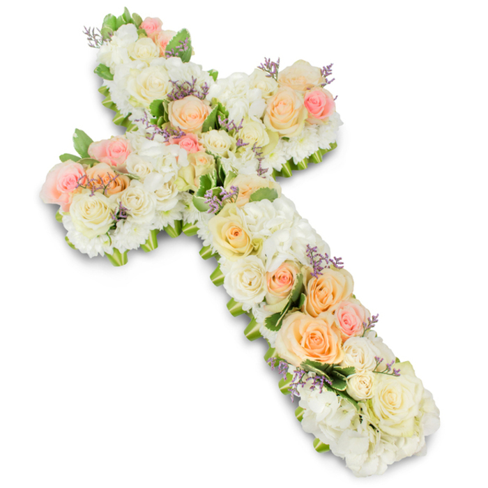A meticulously arranged floral cross is displayed flat against a clean, radiant white background, its outline softened by a lavish covering of pastel blooms that radiate calm and reverence. The structure of the Christian cross is completely hidden beneath layers of flowers, creating a continuous, quilted surface of petals that invites the viewer to trace its shape with their eyes. Throughout the design, premium roses in white, ivory, pale peach, and soft pink are individually placed so that each bloom has space to open, their spiralling centres and velvety petals forming focal points from the top to the base. Between these larger roses, generous mounds of white hydrangea or similarly dense blossoms fill every gap, lending fullness and a downy texture reminiscent of soft clouds. Scattered lightly across the cross, small touches of lavender or pale purple filler flowers add delicate specks of colour, like quiet breaths of fragrance woven into the design. At the edges, discreet hints of fresh green foliage peek out, framing the arrangement with a subtle leafy border that enhances the cross shape without drawing attention away from the pastel flowers. A faint, natural shadow beneath the arrangement gives it dimension against the white backdrop, as though it were gently lifted from the surface. This is the kind of thoughtful sympathy tribute often created for services around Gerrards Cross, perhaps laid near the altar of a local church or placed at a graveside on the outskirts of the village, expressing faith, peace, and heartfelt remembrance. Crafted with the practiced hands of local florists, it offers a quiet, dignified way to honour a loved one's journey and comfort family and friends gathering to say goodbye.