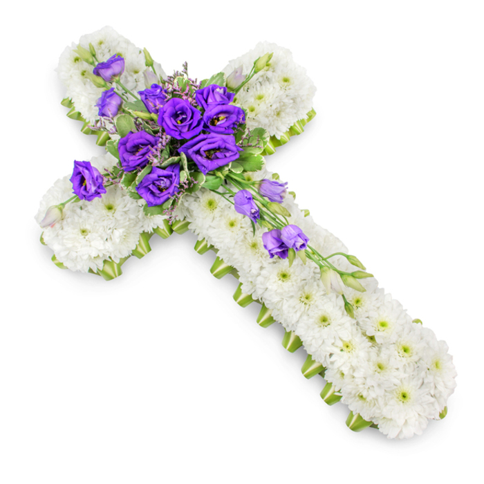 A reverent funeral cross made of fresh flowers is displayed against a bright white background, every detail clearly visible as if laid out on a table before a service at a Gerrards Cross church. The cross is entirely covered with tightly massed white spray chrysanthemums, each bloom small and perfectly formed, their petals overlapping so densely that they create a plush, cushion-like surface. The uniform white is gently broken by the faint green eyes of the chrysanthemums, tiny centres that lend a natural freshness and keep the arrangement from feeling stark. Along the outer edge runs a narrow band of lime-green ribbon, pressed neatly against the sides, framing the cross with a clean, contemporary touch while still remaining respectful and traditional. At the central junction of the cross, a sumptuous cluster of royal purple lisianthus flowers creates a striking focal point. The lisianthus blossoms, with their multi-layered petals and soft, almost satin-like texture, stand in elegant contrast to the crisp white base. Threaded between the purple blooms are tendrils of light green foliage and a few smaller buds, some still tightly closed, others just beginning to unfurl, suggesting the quiet unfolding of remembrance. From this central gathering, a delicate line of lisianthus trails down the vertical arm, gently diagonal, adding movement and drawing the eye along the cross's length. A soft, diffuse shadow beneath the piece lends subtle depth, making it appear as though it rests gently on a polished surface. This floral cross, combining peaceful white and solemn purple, feels especially appropriate for a funeral or graveside tribute in Gerrards Cross, conveying enduring love, faith, and a sense of calm in times of farewell.