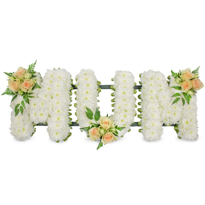 The image shows an elegant floral tribute designed to read MUM in bold, upright lettering, displayed against a stark white background that highlights every detail of the craftsmanship. Each letter is fully covered in immaculate white spray chrysanthemums, packed so densely that they create a smooth, softly domed surface, as if carved from petals alone. The tiny flower heads, each with its own subtle texture and shadow, form a continuous carpet of white that suggests purity, innocence, and quiet reverence. Along the outside edges and within some of the inner curves, a thin dark green structure and ribbon can be glimpsed, discreetly shaping and supporting the letters without drawing attention from the blooms. To break the expanse of white and introduce gentle warmth, three coordinated clusters of roses have been carefully placed. On the upper left arm of the first M sits a bouquet of soft peach and blush pink roses, some fully open, others just beginning to unfurl, mingled with buds and light, lacy greenery. A second, matching cluster rests at the lower centre of the U, tipping slightly forward as though offering a quiet bow of respect. The final grouping, echoing the first, adorns the upper right of the second M, completing the visual flow. The roses' warm tones and fresh foliage provide a comforting contrast to the chrysanthemums' calm whiteness. This style of floral lettering is often chosen by families in Gerrards Cross to pay a tender tribute to a mother at a funeral or memorial service, reflecting both heartfelt loss and enduring affection.
