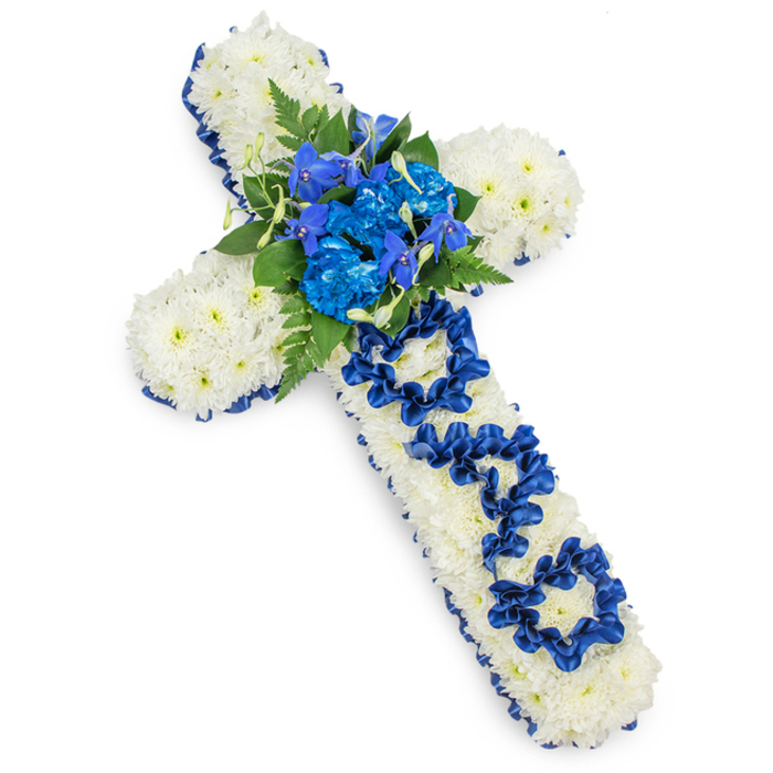 A beautifully composed funeral flower cross, photographed against a bright white background, showcases the careful craftsmanship of a traditional sympathy tribute. The cross shape itself is built entirely from compact white spray chrysanthemums, their small, rounded heads tightly clustered so that no gaps in the base are visible. This dense covering gives the impression of a soft, white blanket, creating both visual fullness and a comforting, pillow-like texture. Around the entire perimeter of the cross, a royal blue satin ribbon runs in a smooth, unbroken line, hugging the curves of each arm and the longer vertical stem. The ribbon has a gentle sheen, and its deep cobalt tone brings a striking contrast to the pure white flowers, suggesting calm dignity and quiet strength-qualities often associated with a much-loved father from the Gerrards Cross community. At the precise centre where the arms cross, a luxuriant spray of blue flowers forms the focal point: richly coloured, ruffled blue carnations or possibly dyed chrysanthemums sit at the heart, while more slender blue blooms-similar to delphiniums or orchids-rise gracefully among them. These are framed by dark green fern fronds and broader leaves, which add layered texture and bring a sense of natural woodland greenery, reminiscent of walks through places like nearby Austenwood. On the vertical section of the cross, the word DAD is clearly spelled out using the same royal blue ribbon, each letter crafted from loops and folds that rest gently over the white chrysanthemum bed. This personalised detail turns the design into a spoken tribute without words, a gentle declaration of love and remembrance. Overall, the arrangement feels serene and reverent, ideal for a service, chapel display, or graveside tribute in Gerrards Cross, conveying enduring affection, faith, and gratitude for a treasured father figure.