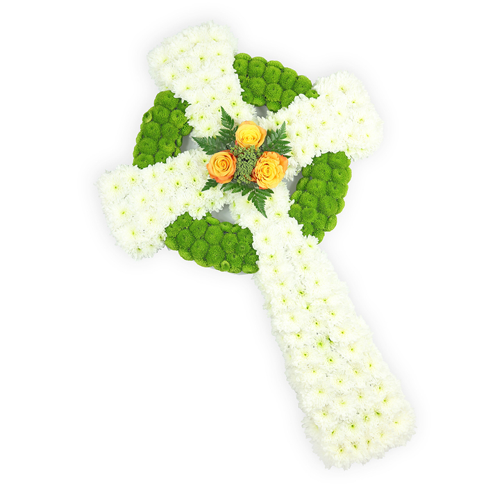 Set against a luminous white background and photographed from a slightly elevated viewpoint, this handcrafted floral Celtic cross reads as both a work of art and a solemn emblem of remembrance. The cross's primary structure is fashioned from dense clusters of small white spray chrysanthemums, their soft, layered petals creating an even, cloud-like surface that suggests purity and the quiet of memory. Accenting that purity are sections of vivid apple-green button chrysanthemums, tightly grouped to form the ring at the intersection of the arms and to provide alternating panels along the horizontal arms; these green clusters give the cross a plush, almost mosaic texture, and they define the traditional circular element of Celtic symbolism with contemporary clarity. At the meeting point of the arms sits a trio of sunlit orange-yellow roses, fully open and carefully arranged to form a warm focal nucleus; a few sprigs of deep green foliage cradle them, lending a restrained natural contrast. The lighting gently highlights petal detail and the design's dimensional contours, so the cross appears sculptural and balanced. For families in Gerrards Cross and neighbouring villages such as Iver or Burnham, this arrangement offers a respectful funeral or memorial tribute that subtly evokes Irish roots without overpowering the solemn tone of a service. The overall effect is one of dignified craftsmanship: a floral statement that honours faith, heritage, and enduring love with considered texture, colour, and compassionate presence.