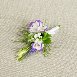 A single, thoughtfully designed boutonniere rests on a pale beige, linen-like cloth, its subtle weave adding a soft, natural backdrop to the delicate flowers arranged on top. At the centre of the composition sit two lisianthus blossoms, their petals a luminous white with intricate, ruffled edges painted in rich purple, giving them the look of miniature watercolour blooms. Around them, clusters of tiny, crisp white filler flowers evoke the delicacy of baby's breath, filling the spaces with a gentle haze of lightness and creating an airy cushion for the focal blooms. Rising gracefully from the cluster is a slender stem of small, bell-shaped florets in a saturated, grape-purple shade-very much like muscari or grape hyacinth-adding height, texture, and a deeper thread of colour. Fine, fern-like greenery arcs and curls around the flowers, its feathery texture recalling the fresh, cool foliage you might find along the leafy paths near Bulstrode Park in Gerrards Cross. Two pale green buds, still tightly closed, are tucked into the design, lending a sense of new beginnings and the quiet anticipation that surrounds a wedding morning. The stems at the base are aligned with care and wrapped in smooth white satin ribbon, the fabric folded tidily and finished with a small, elegant bow that sits snugly against the stems, ready to be pinned securely to a jacket. The lighting in the scene is gentle and even, enhancing the soft whites, vivid purples, and fresh greens without harsh shadows, creating a calm, timeless feeling. It is the sort of refined floral detail a local florist would prepare for a groom, best man, or prom guest heading out across Gerrards Cross for an important, memory-making occasion.