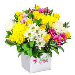In this image, a lush, rounded bouquet overflows from a minimalist white cube-shaped box, the clean background allowing every petal and leaf to stand out in sharp detail. The flowers are densely packed, creating a rich tapestry of colour built around glowing yellow tones, crisp whites, and deep magenta accents. Large yellow chrysanthemums, with their finely layered petals and velvety texture, sit alongside clusters of small yellow roses, some in tight buds and others just beginning to unfurl, suggesting warmth and optimism. Interwoven between them are fresh white daisy chrysanthemums with bright green eyes that lend a casual, garden-fresh charm, while fuller white blooms help soften the overall silhouette. Vibrant fuchsia and raspberry-hued chrysanthemums bring a vivid pop of colour, their slightly ruffled petals drawing the eye through the arrangement. Small blush-pink and yellow rosebuds are scattered thoughtfully, adding delicate touches of romance and detail. Dark green, glossy foliage surrounds and supports the blossoms, especially at the base, grounding the bouquet and highlighting the brightness of the flowers above. The white box, with its smooth, matte surface and straight edges, gives the composition a modern, gift-box feel, as if ready to be carried down by a florist from Station Road to a doorstep in central Gerrards Cross. The overall impression is one of joyful abundance and contemporary elegance, ideal as a centrepiece for a kitchen table or as a cheerful surprise sent to friends and family across Gerrards Cross and nearby Chalfont St Peter.