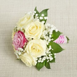 In the heart of Gerrards Cross, a bouquet graces a warm, neutral linen, embodying both romance and local sophistication. Creamy white roses with elegantly unfurling petals form the bouquet's core, their freshness evoking an early summer morning along the green lanes of the Buckinghamshire countryside. Amid this serene canvas, a single vibrant magenta-pink rose glows just off-centre-a focal point brimming with joyful energy, reminiscent of a celebratory toast at a wedding gathering near the Gerrards Cross Memorial Centre. Baby's breath, delicate and ethereal, intertwines among the roses, offering gentle texture and the whisper of classic bridal tradition. Deep green leaves accent the blooms, their smooth surfaces a natural contrast to the softness of each petal. The bouquet's stems, neatly bound in bright pink satin ribbon, are adorned with a graceful, spiraling strand of pearly beads, lending a contemporary twist to this timeless floral design. Soft, filtered daylight bathes the arrangement, revealing intricate textures and subtle color gradations. The bouquet's scent-a blend of fresh roses and leafy greenery-evokes nostalgia, echoing garden paths and cherished celebrations in Gerrards Cross. This exquisitely arranged bouquet is ideal for commemorating life's milestones, from elegant wedding ceremonies to heartfelt anniversaries, seamlessly blending expert floral craft with vibrant local character.
