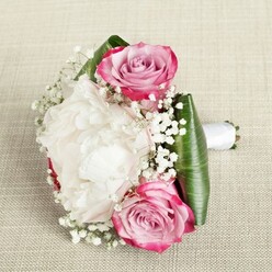 Bathed in gentle daylight, this bridal bouquet unfolds warmly against a neutral linen background reminiscent of refined gatherings in Gerrards Cross' tranquil neighbourhoods. Its composition is driven by a central, plush white peony, petals unfurling in creamy cascades that seem to breathe softness into the entire piece. Framing this cloud of elegance, two extraordinary pink roses appear almost suspended among the blooms-their petal edges alive with fuchsia and magenta, while their cores dissolve to blush and faint lavender, evoking the delicate transition from dawn to morning on a peaceful street off Packhorse Road. Ethereal baby's breath drifts between the flowers, its tiny white stars lending the bouquet a sense of light, joyful movement-much like laughter drifting through a garden marquee at a Gerrards Cross wedding. The arrangement's perimeter features striking, deep green leaves, meticulously shaped and folded with a professional touch, casting a strong, fresh border that highlights the interplay of colours within. Securely held by a smooth, bright white satin ribbon, the bouquet's handle poses gracefully to the side, inviting the recipient to grasp a moment of hope and celebration. Every bloom seems chosen with love and expertise, conjuring images of wedding mornings in Gerrards Cross and the promise of a day filled with cherished memories. This arrangement is an inspired choice for bridesmaids or romantic gifts, handcrafted by local florists proud to serve their community.