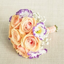 Crafted with thoughtful artistry by a talented florist in Gerrards Cross, this bridal bouquet harmonizes tradition with a touch of modern flair. Each sumptuous rose-painted in tones of peach, apricot, and creamy blush-broods softly against the light cream linen backdrop, their velvety petals reminiscent of early blooms seen along Packhorse Road in spring. Punctuating this warm palette, ruffled Lisianthus blossoms bring a spark of white and dramatic violet edges, adding both movement and visual intrigue, much like the changing colours surrounding Bulstrode Park. Baby's Breath, airy and light as whispers, brings together each element, its delicate clusters reminiscent of gentle morning fog drifting over Gerrards Cross fields. The bouquet's stems, expertly bound and cloaked in a peach-hued satin ribbon, offer a luxurious tactile finish, accented with gleaming white pearls thoughtfully arranged for a final nod to romance. This composition feels as if it would be at home in the hands of a smiling bridesmaid walking through St. James Church, or as a centrepiece awaiting celebration at a family gathering nearby. The entire arrangement captures the joy and anticipation of special days in Gerrards Cross, evoking emotions of hope, love, and timeless elegance.