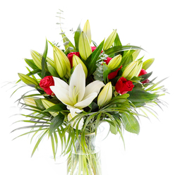 This photograph presents a carefully balanced bouquet topped by a single, fully open creamy-white Oriental lily, placed marginally forward so its pristine, curved petals and pale yellow stamens draw the eye. Surrounding it are numerous lime-green and soft-yellow lily buds-some tightly closed, others showing the first promise of bloom-creating a sense of growth and layered rhythm. Woven among these are velvety red rosebuds and small roses, their deep crimson lending classic romance and dramatic punctuation against the lighter tones. The floral mass is anchored by varied foliage: glossy, dark green lily leaves that offer structure; long, feathery palm fronds in a bright emerald that spill outward with movement; and cool, rounded eucalyptus stems whose silvery-green leaves provide gentle contrast. The stems rest in clear water inside a plain cylindrical glass vase, visible through the transparent vessel, and the arrangement is photographed against a crisp white background that highlights colour, contour, and texture. If you could smell it, the powdery sweetness of the lilies would mingle with the richer, rose-sweet perfume-an aroma that suggests both celebration and intimate devotion. Crafted with a local eye, this arrangement suits anniversaries, congratulations, or a refined sympathy tribute, and is the kind of offering Flower Delivery Gerrards Cross prepares for same-day delivery across Gerrards Cross town centre and nearby streets around the station. The overall effect is one of freshness, considered composition, and timeless emotional clarity, described here as a florist would to someone who cannot see the image but can feel its intent.
