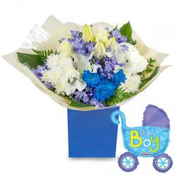 A tender, quietly jubilant bouquet presented in a matte royal-blue square box, paired with a smiling baby-carriage foil balloon that floats to the right and reads "It's a Boy" in bright yellow and lime-green letters. The visual story begins with elegant white roses nested at the center, ringed by large white lilies-some still tight as buds-and full, cushiony white chrysanthemums that give the arrangement its soft, classic base. Interspersed are vibrant electric-blue chrysanthemums and a standout cluster of deep azure blooms that create a contemporary focal point, while small lavender-periwinkle clusters, suggestive of hyacinths, weave through the stems to add a delicate, nostalgic scent and fine texture. The greens are abundant and varied: broad glossy leaves, slender fern fronds, and fresh, herbaceous sprigs that provide structure and a cool contrast to the pale petals. The bouquet is wrapped in cream-coloured textured tissue gathered at the box's lip, the folds of paper catching light and implying the faint rustle of wrapping. To the right, the pram-shaped balloon is rendered in pale blue with darker blue trim, polka-dot accents and tiny hearts around the wheels; its reflective foil surface picks up room light and adds a celebratory shimmer. The overall mood is one of gentle excitement and caring craftsmanship-an arrangement I would deliver myself for a newborn welcome in Gerrards Cross or to congratulate new parents at a nearby home on Vicarage Road or a quiet street near Burnham Beeches, a floral message of warmth and fresh beginnings.