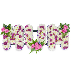This heartfelt tribute spells MUM in three substantial, three-dimensional letters, each formed from a dense mass of pure white chrysanthemum blooms that create a soft, cushiony surface and a soothing visual silence. Scattered through that snowy foundation are clusters of deep purple and magenta pom-pom blooms, perfectly spaced to provide subtle patterning and tonal depth. Vibrant pink spray roses punctuate the design as focal accents: two to three bright roses nestle into the upper left of the first M, a larger cluster of four to five roses and luxuriant fern leaves sits within the lower curve of the U, and a matching small rose cluster adorns the upper right of the final M. Rich dark green foliage, including feathery fern fronds, frames each bouquet, while tiny blue accent flowers peek out like soft notes of colour among the leaves. A discreet dark bar links the letters across the base, lending structure without distractive hardware, and a slim purple ribbon along the outer edges subtly sharpens each letter's form. Styled under soft studio light, the arrangement conveys both the quiet of mourning and the warmth of remembrance-an ideal tribute for a funeral, memorial or celebration of life. Flower Delivery Gerrards Cross prepares pieces like this with close attention to texture and proportion, serving families across the High Street, around the station and into neighbouring Beaconsfield and Chalfont St Peter with sensitive, local care.