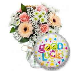 A supportive, celebratory gift set captured against stark white: on the left a full bouquet stands in a clear glass vase tied with natural twine, the tactile knot giving the design a handcrafted finish. The blooms pair soft peach and pale pink roses-velvety and romantic-with vivid peach-orange Gerbera daisies whose dark brown centres offer a concentrated, almost chocolate-brown texture at their heart. Wisps of white baby's breath (Gypsophila) breathe through the arrangement like meadow lace, while clusters of small white and lime-green chrysanthemum-like florets introduce a crisp, lively note. Rich green foliage frames the composition, creating depth and a cooling green undercurrent to the roses' gentle scent. To the right, overlapping the lower bouquet, is a shiny silver Mylar balloon that captures light and draws the eye; it's decorated with scattered bright stars, hearts and confetti shapes in blue, pink, yellow and orange. Prominently across its face, the message Good Luck! is rendered in a chunky, cheerful, multi-coloured typeface, with the two 'o's cleverly replaced by yellow smiley faces-one winking, the other playfully sticking out its tongue-and a tiny KALEIDOSCOPE logo at the base. This composition feels optimistic and intimate, an ideal pick-me-up for someone leaving for a new job, sitting an exam, or moving house. As Flower Delivery Gerrards Cross, we imagine this being sent for same-day local delivery around Gerrards Cross, Little Chalfont or Beaconsfield to offer a bright, fragrant boost.