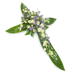 Presented against a pristine white backdrop and viewed from a soft overhead angle, this floral cross is a careful study in texture and restraint, rooted in lush tropical foliage. Large, gleaming green Ti leaves create the defined vertical and horizontal arms, their smooth, veined surfaces folded and layered to form a steady, protective frame. Concentrated at the centre and flowing outward along each arm are clusters of creamy ivory and pure white lisianthus, their ruffled petals and partially closed buds lending a feeling of gentle unfolding. Small white chrysanthemum-like blooms provide compact brightness among the lisianthus, while sprays of tiny lavender or pale purple limonium (or asters) scatter across the design like breath, adding soft contrast and subtle depth. Wisps of delicate green filler foliage are woven through the flowers to create a natural cadence between the glossy greenery and the petals' softness. The overall lighting is soft and neutral, accentuating the arrangement's serene palette and the tactile contrast between waxy leaves and feathery blooms. As a local florist serving Packhorse Road, the railway station area, and nearby Chalfont St Peter, Flower Delivery Gerrards Cross prepares this piece for funeral chapels, memorial services, and bedside remembrances; its shape and colouring offer a clear religious symbol while conveying peaceful dignity. The composition communicates quiet consolation-an unspoken embrace for mourners-balanced between permanence in the green structure and the fragile grace of the flowers.