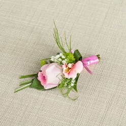 Like a quiet love story woven from the gardens of Gerrards Cross, this handcrafted boutonniere invites the senses with its delicate composition and soft, harmonious colors. At its center lies a blushing pink rose, petals tender and tightly curled, promising youthful beauty and subtle emotion. Alongside, a pale, peach-tinted alstroemeria blossom reveals inner flecks of golden yellow and dark speckles, adding both intrigue and a sun-kissed warmth reminiscent of morning walks through West Common fields. Clusters of fine white baby's breath nestle among the focal blooms, their delicate airiness balanced by rounded mounds of vivid green cushion chrysanthemums-each adding depth, freshness, and tactile delight. Foliage, both spiky and broad, is artistically layered: slender blades and wispy fern-like fronds spring upwards, while broad, folded leaves form a supportive base, shaped with a master florist's touch. Winding around the stems is a lustrous fuchsia satin ribbon, tied into a neat, celebratory bow-a pop of color reflecting both joy and sophistication, like a secret signature of local festivities. Presented upon a neutral, textured fabric whose subtle warmth calls to mind beloved spaces in Gerrards Cross, this boutonniere embodies love's quiet beginnings and moments worth remembering. Whether destined for a wedding at the epic St. James's Church or a celebratory gathering with friends, it expresses style, sincerity, and a connection to the local landscape, crafted for those who appreciate beauty stitched into every detail.
