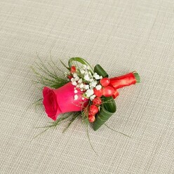 An elegant groom's boutonniere rests on a pale beige, woven fabric backdrop, the subtle grain of the material lending a soft, homely feel, like a linen runner you might see at a Gerrards Cross marquee reception. The focal point is a single, saturated fuchsia pink rosebud, its velvety petals wrapped in tight concentric layers at the centre and opening outwards at the edges to reveal a lush, almost luminous depth of colour. Nestled closely around the rose, airy clusters of white baby's breath create a delicate halo, each tiny bloom catching the light and giving a cloud-like softness that balances the boldness of the rose. Scattered through this white mist are glossy, bright red hypericum berries, their rounded forms adding texture and a playful, seasonal accent, reminiscent of festive gatherings in homes near East Common or along Packhorse Road. Slender, feathery fronds of green foliage spill gently from the sides, lending movement and a natural, garden-fresh feel, while broader dark green leaves are artfully folded back, framing the rose like sculpted wings and providing a dark contrast that makes the central colour pop. The stems are tightly wrapped in a smooth, rich red satin ribbon, which is finished with a small, neat bow, its sheen hinting at candlelight and polished shoes on a wedding morning. The lighting is soft and even, with gentle shadows that emphasise the layers of petals and overlapping leaves, as though the piece has just been placed down by an experienced florist to be checked before delivery. Crafted with the care you'd expect from a specialist serving weddings and proms throughout Gerrards Cross, this compact floral design conveys romance, celebration, and a tailored elegance perfect for lapels at church ceremonies, registry offices, or stylish local venues.