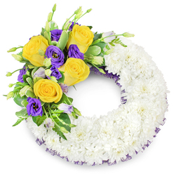 This sympathy wreath presents itself as an artfully assembled ring of pristine white spray chrysanthemums, their tightly layered petals forming a continuous soft surface that suggests unity and repose. The white foundation is deliberately neutral and serene, a backdrop that allows the upper-left floral spray to breathe and speak: several rich yellow roses, fully unfurled in shades of lemon, butter and warm candlelight, sit beside clusters of deep royal purple lisianthus whose ruffled, cup-like forms bring velvet contrast. A handful of pale lavender and green lisianthus buds peek through, hinting at unfolding life and adding delicate textural rhythm. Lush green foliage-glossy oval leaves, slighter variegated stems and fine fern fronds-threads through the cluster, giving structure and a natural, garden-fresh feel. Along the inner and outer rims of the chrysanthemum ring a dark purple mesh or crinoline trim is discreetly visible, tying the whole piece back to the purple blooms and lending a subtle, refined finish. The composition is balanced so the wreath reads as both respectful and quietly warm, appropriate for a funeral chapel, family memorial at St. Mary's or a graveside service in the Gerrards Cross area. The cool satiny lisianthus, the soft citrus of yellow roses and the whisper of greenery together create a design that offers consolation; it's the kind of floral tribute that speaks softly of remembrance, peace and compassionate presence.