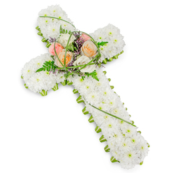 A serene and reverent floral cross is displayed against a spotless white background, its form immediately recognisable as a symbol of faith and remembrance. The cross is fully covered in hundreds of small, pure white chrysanthemums, carefully placed side by side so that no gaps show, creating a soft, cushion-like surface that feels calm and comforting even from a distance. The edges of the cross are precisely finished with a ribbon of bright green foliage, wrapping neatly around the outline and giving the design a defined, almost sculpted edge. At the central intersection of the cross, a beautifully balanced focal spray introduces gentle colour and movement. Several full-headed roses in warm shades of peach and pale blush pink, mingled with creamy white roses, sit at the heart of the design, their layered petals opening in soft spirals. They are surrounded by feathery green ferns, slender arcs of glossy green grass, and delicate touches of tiny purple filler flowers that peep through, adding a nuanced, almost whispered note of contrast. The arrangement is lit in a way that feels like natural daylight, bringing out the softness of the whites and the freshness of the greens without any glare. This floral cross would be perfectly at home at a funeral or memorial gathering in Gerrards Cross, perhaps following a service before being carried to a peaceful graveside. It offers a quiet, dignified way to say goodbye, reflecting both Christian symbolism and the gentle, leafy character of this Buckinghamshire town, with flowers arranged as carefully as any tribute created by a trusted local florist.