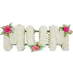 The image portrays an elegant sympathy flower tribute spelling out MUM in large, capital block letters, resting against a simple white backdrop that lets every detail stand out clearly. Each letter is completely enrobed in masses of small white chrysanthemum blooms, their petals tightly layered to create a soft, pillowed effect that speaks of purity, peace, and respect. The uniform carpet of white makes the word highly legible, with gently rounded edges that soften the strong letter shapes. Beneath the flowers, a dark green frame or ribbon peeks discreetly along the lower edges, giving the tribute a neat finish and a sense of depth, as if the letters are gently lifted from the surface. Adding warmth and a tender focal point, three identical floral accents in vibrant pinks are arranged across the design. On the upper left arm of the first M, a bright fuchsia garden rose opens in full bloom, hugged by blush-pink spray roses and elegant sprigs of fine green fern. A second cluster is nestled into the lower centre of the U, drawing the eye towards the heart of the word, while a third sits proudly on the upper right of the final M, completing a graceful diagonal flow of colour. The interplay of crisp white, vivid fuchsia, and fresh greens creates a tribute that feels both classic and contemporary. It is the kind of thoughtful memorial piece a local Gerrards Cross family might choose to accompany a farewell service or a burial in the surrounding Chiltern countryside, expressing unspoken affection for a cherished mother in a gentle, floral language.