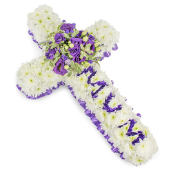 This substantial Christian cross is lovingly formed from countless white chrysanthemums, each bloom tightly nestled to create a soft, cushion-like surface that reads as purity and repose. The whole cross is outlined with a ruffled band of rich purple satin, a border that lends solemnity and a refined silhouette against the studio's white background. On the vertical shaft the letters MUM are precisely rendered in smaller purple flower heads-likely lisianthus or petite spray chrysanthemums-so the personalised tribute is immediately visible and heartfelt without disrupting the clean geometry of the design. The carefully chosen contrast between white and purple balances reverence with a personal intimacy.

Where the arms meet, a generous central spray becomes the arrangement's focal heart: deep violet roses, softer lavender roses and ruffled lisianthus combine to form a lush, layered bouquet that feels both opulent and consoling. Variegated foliage with pale margins and darker centres, plus a few green berries, introduce tactile depth and gentle colour variation, their freshness reminiscent of early-morning walks near Gerrards Cross station and Denham Country Park. The scent is quietly floral-powdery chrysanthemum undercut with the warm, rounded perfume of roses-creating a mood of reflection. Prepared to support families across Gerrards Cross and neighbouring Chalfont St Peter, Flower Delivery Gerrards Cross offers this design for funerals, memorials and funeral home display, where it reads as a respectful, enduring expression of love and farewell.