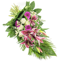Set against a spotless white background, this elegant sympathy sheaf stretches diagonally like a gentle sigh, from the bound stems at the top left down to a tapered point at the bottom right. At its heart, several magnificent Stargazer lilies command attention, their star-shaped blooms painted in rich fuchsia-pink with clean white borders and dark burgundy speckles, a dramatic yet tender tribute reminiscent of the thoughtful arrangements often chosen for services in Gerrards Cross. Some buds remain closed, soft green and blush-pink at the tips, promising beauty still to come. Nestled among them are luminous magenta gerbera daisies, which introduce a note of warmth and affection, while creamy white roses and fluffy white carnations provide a soothing counterpoint, their petals tightly layered and velvety to the touch. Tiny clusters of white daisy-like flowers are scattered throughout, like little breaths of light, adding airiness and delicate detail. The entire spray is cradled in lush green foliage: broad, glossy leaves give the design structure, feathery ferns add depth and texture, and long, arching grassy blades extend outwards, reinforcing the sense of gentle motion. The stems are carefully gathered and secured at one end, clearly showing the skilled hand of a florist preparing a respectful final farewell. This arrangement feels calm and contemplative, ideal for resting beside a casket or being delivered to a memorial service near the quiet residential streets off Packhorse Road, offering comfort, beauty, and a deeply personal expression of sympathy within the Gerrards Cross community.