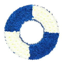 A beautifully composed floral wreath, designed to resemble a classic maritime lifebuoy, rests against a bright white background, its colours recalling the cool clarity of a lake on the edge of Gerrards Cross. The wreath forms a flawless circle with a hollow centre, every inch of its surface packed tightly with small chrysanthemums or similar button-headed blooms. The flowers are arranged in four defined segments that alternate between saturated royal blue and immaculate white, so that blue and white quarters meet cleanly at precise, invisible seams. The blue sections feel deep and velvety, their compact petals overlapping like tiny waves, while the white sections bring a sense of stillness and light, as if catching soft daylight filtering over nearby East Common. A narrow, dark blue ribbon trims the inner edge of the ring, gathered in delicate ruffles that create a gentle shadow line and add a refined, handcrafted detail. The overall impression is one of balance and care: no stems are visible, just a smooth, undulating carpet of blossoms that invites the fingertips. Emotionally, this funeral wreath speaks of calm strength and dependable support, a floral 'lifeline' offered in a time of loss. It is especially fitting as a tribute for someone with a maritime calling, naval background, or a love of boating and the outdoors, yet it also reads more broadly as a symbol of someone who was a steady, saving presence in their family or community. Created by skilled local florists serving Gerrards Cross and the surrounding villages, the piece would sit beautifully beside a coffin, at a memorial table, or on a stand by the chapel doors, offering guests a serene, sea-inspired farewell.