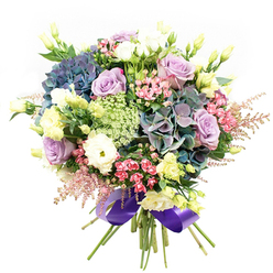 Beautifully arranged by a skilled Gerrards Cross florist, this bouquet captures the essence of local elegance and natural splendour. At its heart lies a flourish of lush hydrangeas in an array of deep, shifting shades-indigo, teal, and dusty purple-that anchor the arrangement like clouds drifting over the lawns of East Common. Intertwined among the hydrangeas are roses in the palest lavender and luscious creamy white, each bloom opening wide to reveal delicately curled petals and refined silhouette, reminiscent of cherished garden classics. Soft, ruffled white ranunculus nestle in, their multi-petaled forms adding a gentle, velvety dimension. Bright notes of slender pale yellow eustoma buds peek through, hinting at fresh beginnings. Sprays of vivid fuchsia-pink blooms and ethereal, feather-light astilbe in pastel pink add playful energy and whimsy along the bouquet's edges, echoing the laughter and liveliness of weekend gatherings in Gerrards Cross Memorial Park. The entire arrangement is buoyed by airy, intricate green and white filigree filler flowers, reminiscent of Ammi Majus flourishing on local hedgerows. Broad strokes of glossy dark green foliage bring out the vividness of every petal and blossom. The stems are artfully gathered and wrapped in a wide, gleaming royal purple satin ribbon that wraps the arrangement in a final note of refinement. Ideal for same-day delivery to friends or family celebrating special moments in Gerrards Cross, this floral creation conveys feelings of joy, grace, and heartfelt connection to the local landscape.