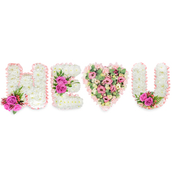 This striking tribute, photographed against a clean white background, spells out H E followed by a heart and U, a bespoke message rendered in floral form with the kind of careful craft we make for clients around Gerrards Cross. The three letters are constructed from dense beds of creamy-white chrysanthemums that create a soft, cushiony surface; their compact heads pick up light and shadow so each serif and curve reads with quiet refinement. Each character is edged with a ruffled blush-pink satin ribbon, a soft border that holds the composition together like a ribbon-bound keepsake. Bright fuchsia-pink roses provide punctuating notes of colour: a twin-rose accent with dusky red berries and deep green ferny foliage grounds the left of the H, a trio of vivid roses crowns the middle bar of the E, and a matching pair finishes the inner right curve of the U. The central heart diverges from the white letters and embraces a romantic, tender palette - layers of soft pink carnations and small blush lisianthus or spray roses, interspersed with pale green eucalyptus leaves that give the heart a cool, textured depth. The overall effect is one of composed devotion: purity and peace from the whites, affectionate warmth from the pinks, and a subtle natural fragrance suggested by eucalyptus and roses. For families in the village or those visiting nearby Chalfont Common, this arrangement - available through Flower Delivery Gerrards Cross for careful local handling - reads as both a loving celebration of life and a personal memorial gesture.