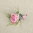 On a calm, light beige background that looks like finely woven linen, a carefully crafted boutonniere lies waiting, as if set aside on a dressing table before a special event in Gerrards Cross. At its heart is a single pink rose, positioned slightly on the diagonal, its petals spiralling inward in a tight, youthful bloom. The colour moves gently from the softest blush at the centre to deeper shades of rose and magenta toward the outer edges, creating a subtle ombré effect that feels both romantic and contemporary. Surrounding this focal bloom, clusters of airy white gypsophila, or baby's breath, scatter like tiny stars, lending a cloudlike softness and a sense of purity. Slender green blades and fern-like sprigs peek out from behind and beneath the rose, adding height, texture, and a hint of the garden, as though freshly gathered from a local Buckinghamshire hedgerow. A glossy, deep green leaf curves snugly around the stem, forming a natural collar that cradles the flower and cradles a few bright droplets of water that catch the light. The stems are bound in a smooth, pastel pink satin ribbon, wrapped with the precision of an experienced florist, and finished with a darker pink bow near the base, creating a refined two-tone effect. The overall look is elegant yet understated, ideal for a groom's lapel at a wedding near Gerrards Cross station, a prom at a nearby school, or any formal occasion where a single, beautifully prepared rose boutonniere speaks quietly of care, commitment, and celebration.