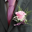 There's a poetic grace in this buttonhole, crafted in Gerrards Cross with a florist's eye for detail and community tradition. A soft pink rose, its velvet petals opening in subtle spirals, anchors the look-fresh, blushing, and unique as dawn breaking over West Common. Around the rose drifts a cloud of feathery baby's breath, lending a breath of airy white that feels both delicate and enduring, just like the friendships that flourish here. Slim arcs of lush greenery frame the composition with a natural, woodland freshness, drawing quiet inspiration from the leafy surroundings of Gerrards Cross Memorial Park. The boutonniere is elegantly tied with a glossy lavender ribbon, shimmering playfully where it fastens to a dark grey lapel. Completing the look, a richly coloured fuchsia tie and patterned grey shirt set a modern yet timeless tone. Soft, indirect daylight highlights the interplay of texture and shade, bringing the palette vividly to life. This creation isn't just floral décor-it's a heartfelt symbol of celebration, making every wearer stand out at weddings, proms, or special gatherings across Gerrards Cross, and reminding us that beauty often lies in the details shaped by local hands.