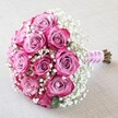 A classic, romantic bouquet graces a softly textured, pale linen surface, its floral artistry unmistakably shaped by the hands of a Gerrards Cross florist. Around a dozen roses take center stage, each bloom striking in its color transition-from a gentle lavender-pink heart to bold, magenta-tinged rims-displaying a lush fullness against a backdrop of airy, pristine white baby's breath. The gypsophila billows between the vibrant roses like morning mists along the Common, lending an ethereal lightness to the overall round, dome-like arrangement. The stems, clearly cut fresh, are wrapped in silky pink ribbon that perfectly matches the blooms, finished with a spiral of delicate pearls for a hint of celebration and tradition. Soft, natural lighting reveals dewdrops on the petals and picks out every thread-like detail of the baby's breath, while the neutral background ensures every nuance of color and texture stands out. This bouquet, which could adorn a wedding at one of Gerrards Cross's historic chapels or brighten an anniversary on Packhorse Road, encapsulates love, elegance, and the enduring artistry of local floral design-ideal for showcasing wedding flower inspirations, event decor trends, or thoughtful romantic gifts in the heart of the community.