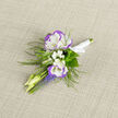 A quiet, refined boutonniere crafted with reverence for texture and season, this piece pairs two lisianthus blooms-snow-white with a pale violet rim-so that their ruffled faces read like small, silk roses. Nestled among them are tiny clusters of baby's breath, their cloud-like presence softening the composition, while the bright, vertical clusters of grape hyacinth provide an arresting blue-violet contrast that lifts the arrangement. Delicate fern fronds weave through the stems, adding a woodland air reminiscent of the paths around Gerrards Cross Common and the verdant edges near the station. Slender, unopened buds offer a hint of optimism and movement, suggesting the floral narrative is still unfolding. The stems are bound in satin ribbon, tied with a discreet knot and set against a neutral linen cloth that makes the colours sing with calm confidence; the linen's texture gives a tactile counterpoint to the lisianthus' velvety petals. There is a soft, green-tinged scent-fresh but not overpowering-that invites a closer breath rather than a bold declaration. Prepared fresh daily in our Gerrards Cross studio and offered by Flower Delivery Gerrards Cross, this boutonniere is conceived for moments of significance: weddings, portraits, or milestone occasions where subtlety and hand-crafted detail matter. The overall effect is one of considered simplicity, a piece that will sit comfortably on a crisp suit lapel and hold its quiet beauty from ceremony through photographs.