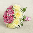 Resting gracefully on a pale, woven fabric that resembles soft hessian or linen, this hand-tied bouquet is captured from a gently elevated angle, allowing the full beauty of its round shape to be seen. The roses are arranged in a striking two-tone design: one half a lush pool of intense fuchsia and magenta-pink blooms, the other half a calm, creamy sweep of light yellow roses. Each blossom is in perfect, full bloom, with spiralling petals that look almost silky to the touch, like something you might carry through a ceremony at a small chapel in Gerrards Cross before heading to a reception nearby. Scattered among the roses, minute clusters of white baby's breath float like airy lace, softening the transitions between colours and giving the bouquet an ethereal, almost cloud-like halo. Here and there, deep green foliage peeks out, framing the roses and adding structure without overpowering the delicate palette. The stems are gathered firmly but elegantly, wrapped in a band of shimmering pink satin ribbon that feels smooth and luxurious. Over this, a single strand of white pearls coils in an even spiral, echoing the spiral of the rose petals and lending a subtle sense of bridal jewellery and heirloom detail. The lighting is soft and flattering, enhancing the gentle contrast between the warm yellows and cool pinks. Crafted with the care you'd expect from a local Gerrards Cross wedding florist, this bouquet feels ideal for a bride, bridesmaid, or romantic anniversary gift, conveying devotion, joy, and a touch of classic glamour.
