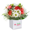 Brimming with the cheerful warmth of a Gerrards Cross afternoon, this striking bouquet is artistically arranged within a crisp white square gift bag that rests gently on a spotless white surface. The generous gathering features a cascade of coral and peach carnations, their plush, frilled petals radiating energy and a soft, inviting fragrance reminiscent of local market days. Each bloom is carefully interlaced with snowy white daisies, whose gold-green centers sparkle with joyful contrast, much like wildflowers dotting the fields near East Common. White baby's breath adds a whimsical, airy charm, its tiny blossoms creating the effect of a floral mist. In a nod to the promise of new growth, a few unopened, purple-touched buds peek through the arrangement's left side, enhancing depth and curiosity. Encircling this vibrant collection, broad deep green leaves create a lush and balanced cradle, supporting the flowers in understated elegance. The arrangement forms a perfectly rounded, abundant silhouette, capturing the spirit of thoughtful gifting that Flower Delivery Gerrards Cross is known for. Presented in a sturdy, easy-to-carry gift bag with elegant ribbon handles, the bouquet shines against a pure white background-suggesting freshness, high quality, and the happiness that comes with sending a heartfelt gesture to someone close by, whether for a birthday celebration by West Common or an anniversary surprise in Denham.