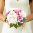 This bridal bouquet appears as a serene, carefully gathered cloud of soft colour, ideal for a refined wedding in Gerrards Cross. At its centre, creamy peonies open in layers of ivory and palest blush, their plush petals forming generous, rounded blooms that seem to glow in the natural light. Nestled among them are roses in tones of dusty pink and muted lilac, each bud at a slightly different stage of opening, adding quiet rhythm to the tightly composed design. Fine sprays of gypsophila drift through the flowers like a gentle mist, creating a sense of airiness and bridal tradition that feels at home in a ceremony near West Common or an elegant reception tucked away off Bulstrode Way. The surrounding foliage is a deep, polished green, its smooth leaves wrapping subtly around the bouquet to frame the flowers and enhance their softness. The arrangement is firmly bound yet looks effortless, as though it has just been lifted from a well-tended garden on a calm spring morning. There is a hushed, contemplative mood in the way the colours blend-nothing harsh, only a soothing palette that echoes the quiet charm of local churches and country-house venues around Gerrards Cross. Crafted with an eye for proportion and texture, the bouquet is perfectly sized to be cradled close to the bride's dress, sending out a message of harmony, grace, and understated romance as she walks down the aisle.