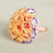 Laid flat on a neutral, textured beige cloth and photographed from just above, this bouquet feels like a soft exhale of affection. At its heart, abundant peach and soft orange roses open in sumptuous, velvety spirals that capture and cradle the light; their warm glow suggests early-morning sun on a quiet Gerrards Cross street. Interspersed among those generous blooms are white lisianthus flowers with frilled petals tipped in a striking violet edge - small theatrical moments that lend crisp contrast and modern sophistication to the overall warmth. The delicate, cloud-like sprays of baby's breath thread through the composition, lending a veiled, airy quality that lightens the visual weight and brings an almost whispering innocence to the piece. The bouquet's handle, visible toward the bottom right, is wrapped in a peachy satin ribbon whose sheen is soft rather than glossy, while a string of creamy pearls coils around it like a memory of family traditions. The textured fabric underlay, perhaps linen or burlap, shows gentle creases that add homely charm and site the arrangement in a tactile setting familiar to local brides choosing flowers for village halls or cottages near Chalfont St Peter. The overall effect is quietly celebratory - romantic, tactile, and refined - an artisan-crafted bouquet suited to intimate weddings, anniversary surprises, or thoughtful gifts that seek a balance of classic beauty and contemporary detail.
