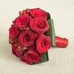 An opulent cluster of approximately ten lush red roses, designed by florists in Gerrards Cross, commands attention with its bold, velvety petals and intense, ruby hues. Each blossom is perfectly formed, their textures enhanced by the daylight softly streaming through a local window. Intermingled are small, bright red hypericum berries, whose slightly glossy surfaces introduce variation and charm, reminiscent of the festive markets in Gerrards Cross. Deep green, broad-leaved foliage is expertly positioned to encircle the roses, forming a sculptural cradle that sets off the vivid red blooms. The bound stems, wrapped tightly with a gleaming red satin ribbon, offer both style and function, their finish hinting at a practiced hand and a loving touch. Set atop a pale, textured linen cloth, the bouquet radiates elegance, its hues intensified by the subtle backdrop. From visual splendour to the evocative scent of fresh roses, the arrangement brings a touch of romance and celebration - perfect for commemorating weddings, anniversaries, or cherished milestones across Gerrards Cross, and available for special delivery to homes and venues throughout the area.